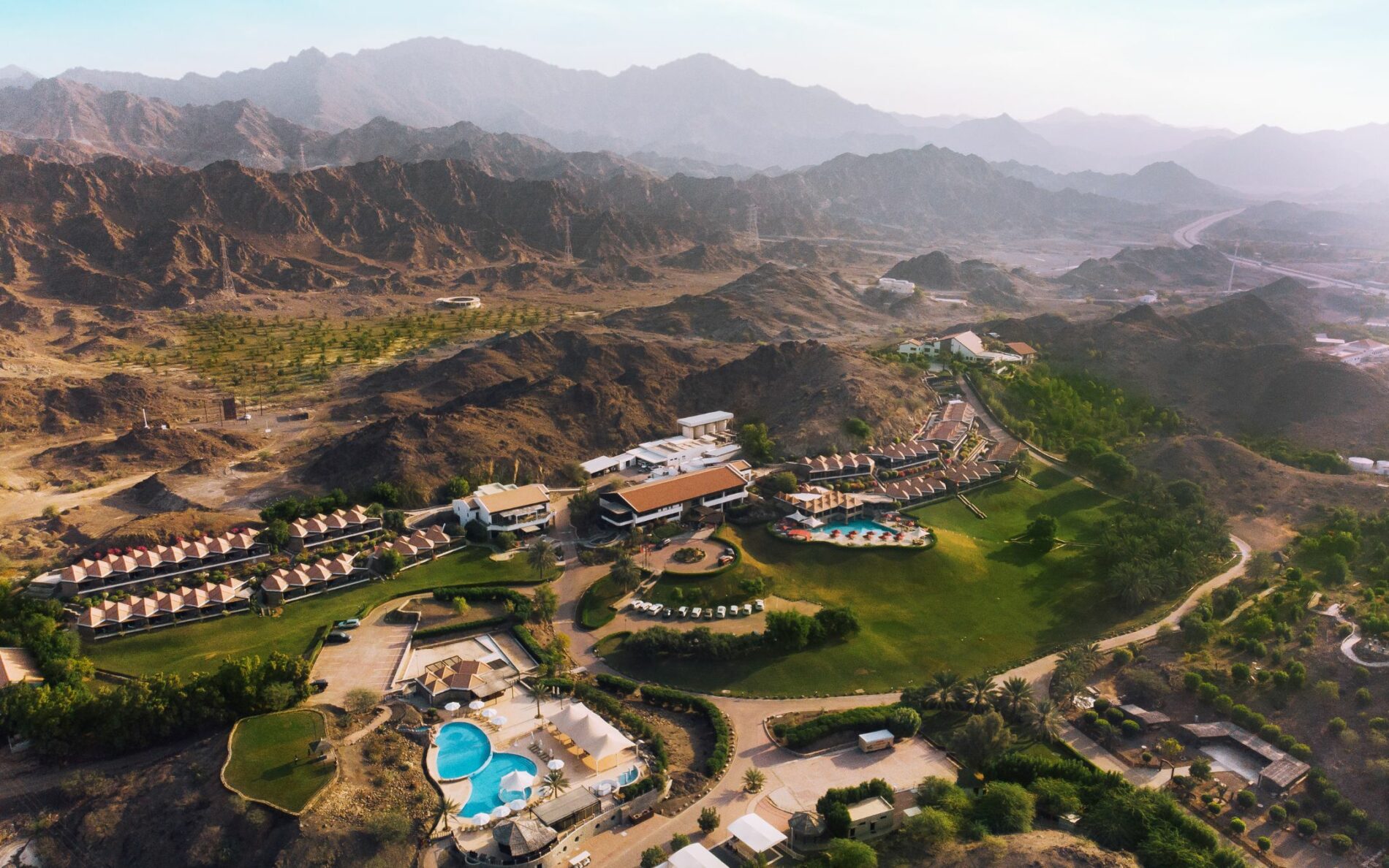 mountains in the UAE with luxury hotel resort with luxury pool. lots of green tress and grass
