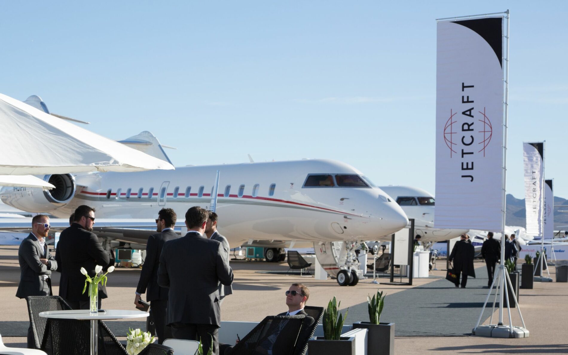 men in suits sat in front of luxury private jets on a sunny day