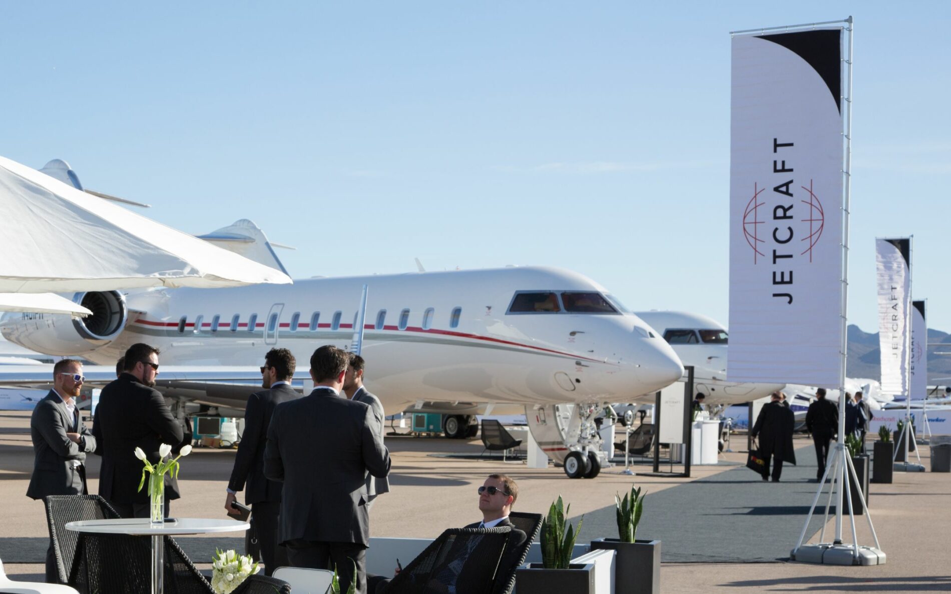 men in suits sat in front of luxury private jets on a sunny day luxury travel lifestyle pr