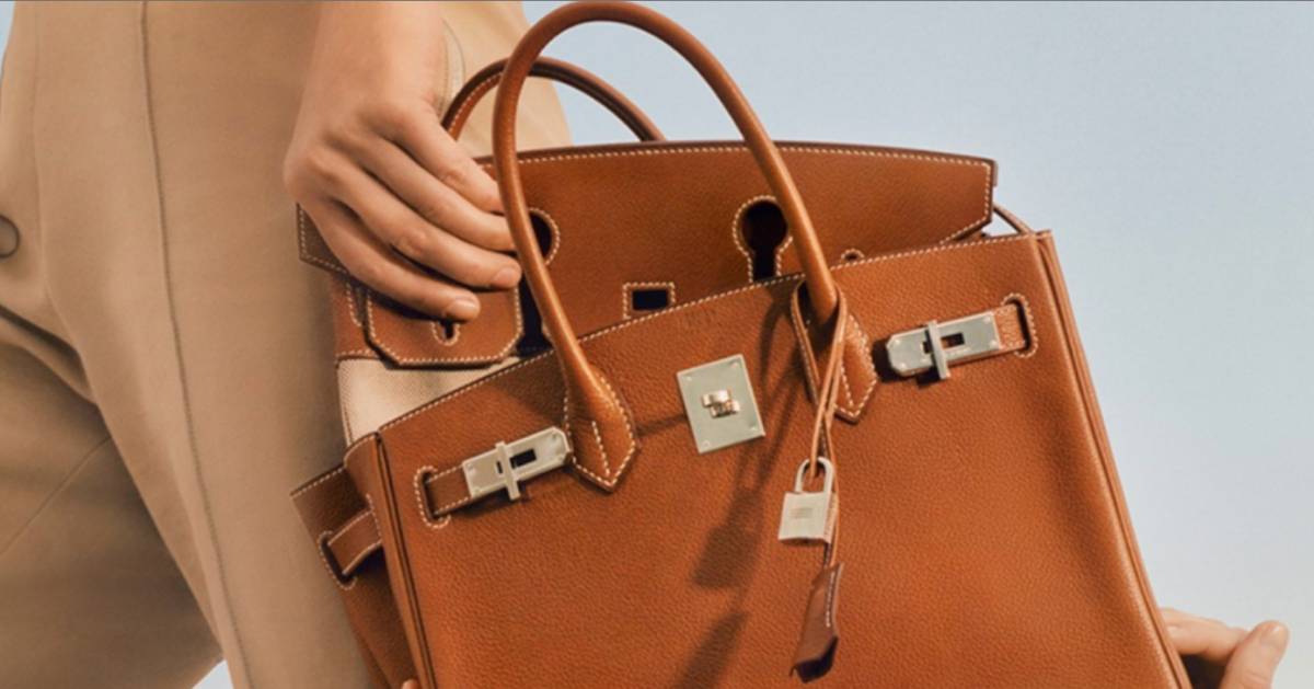 A woman holding an elegant brown leather Hermes Birkin bag with gold-tone hardware.
