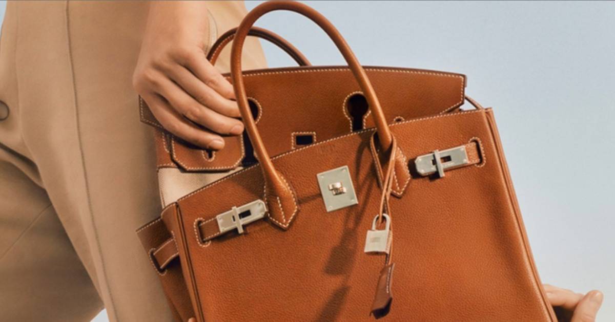 A woman holding an elegant brown leather Hermes Birkin bag with gold-tone hardware.